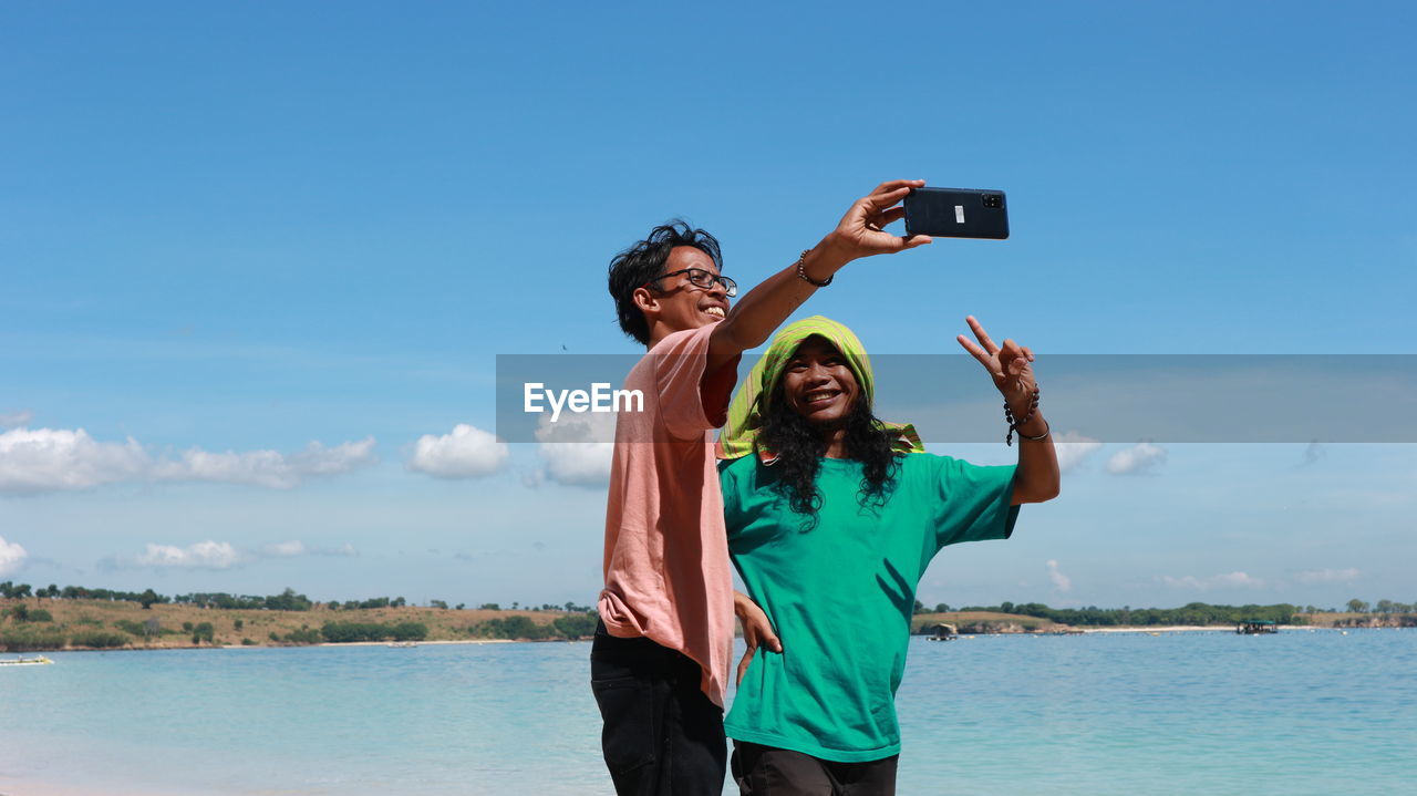 MAN PHOTOGRAPHING WITH ARMS RAISED AGAINST SKY