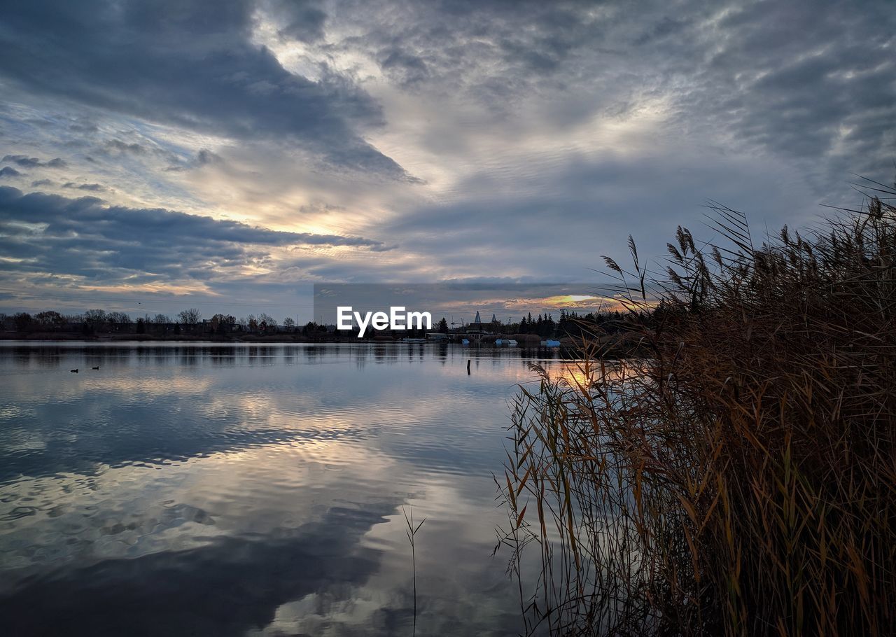 VIEW OF LAKE AGAINST CLOUDY SKY DURING SUNSET