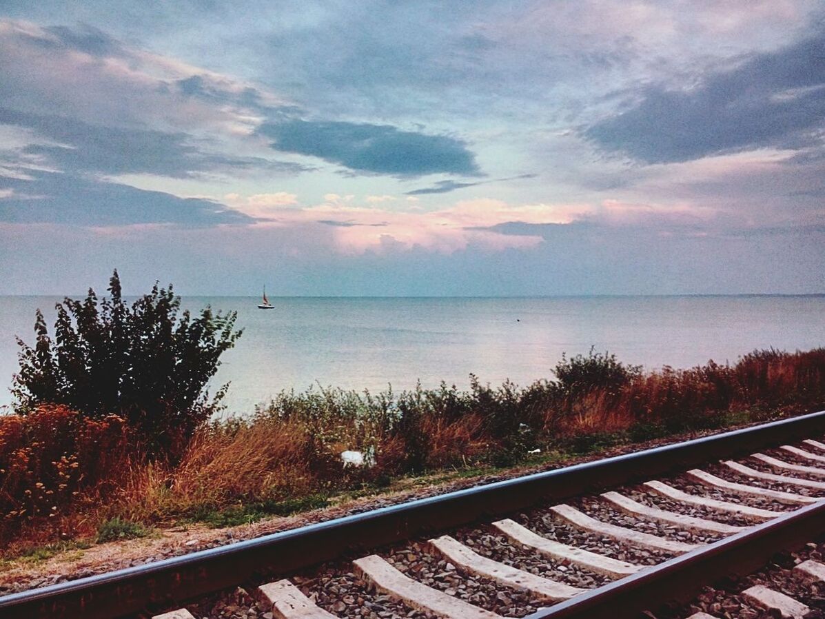 Railroad tracks by sea against sky