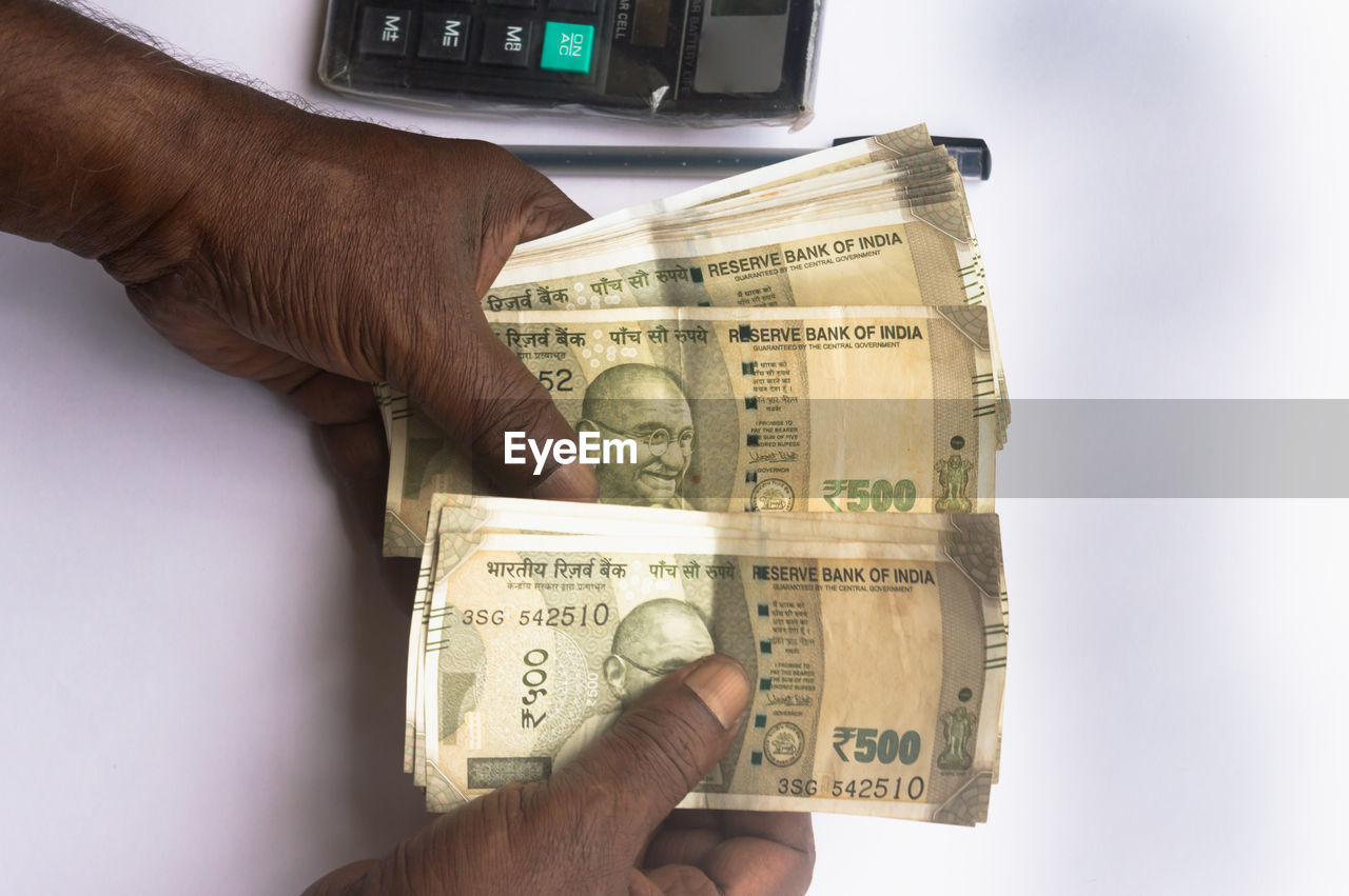 Business man hand counting indian rupee note on table. high angle view. close up. white background.