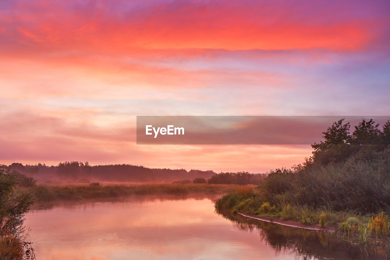 SCENIC VIEW OF LAKE BY TREES AGAINST ORANGE SKY