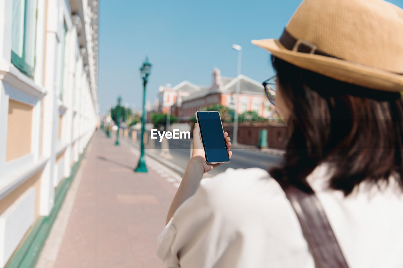 Tourist woman in white shirt and straw hat use mobile or smartphone in old town bangkok, thailand