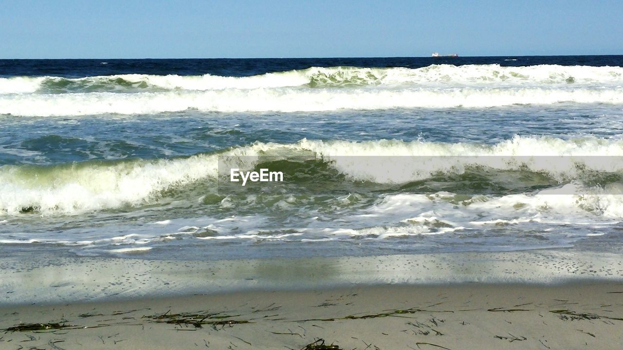 Sea waves on beach against clear blue sky