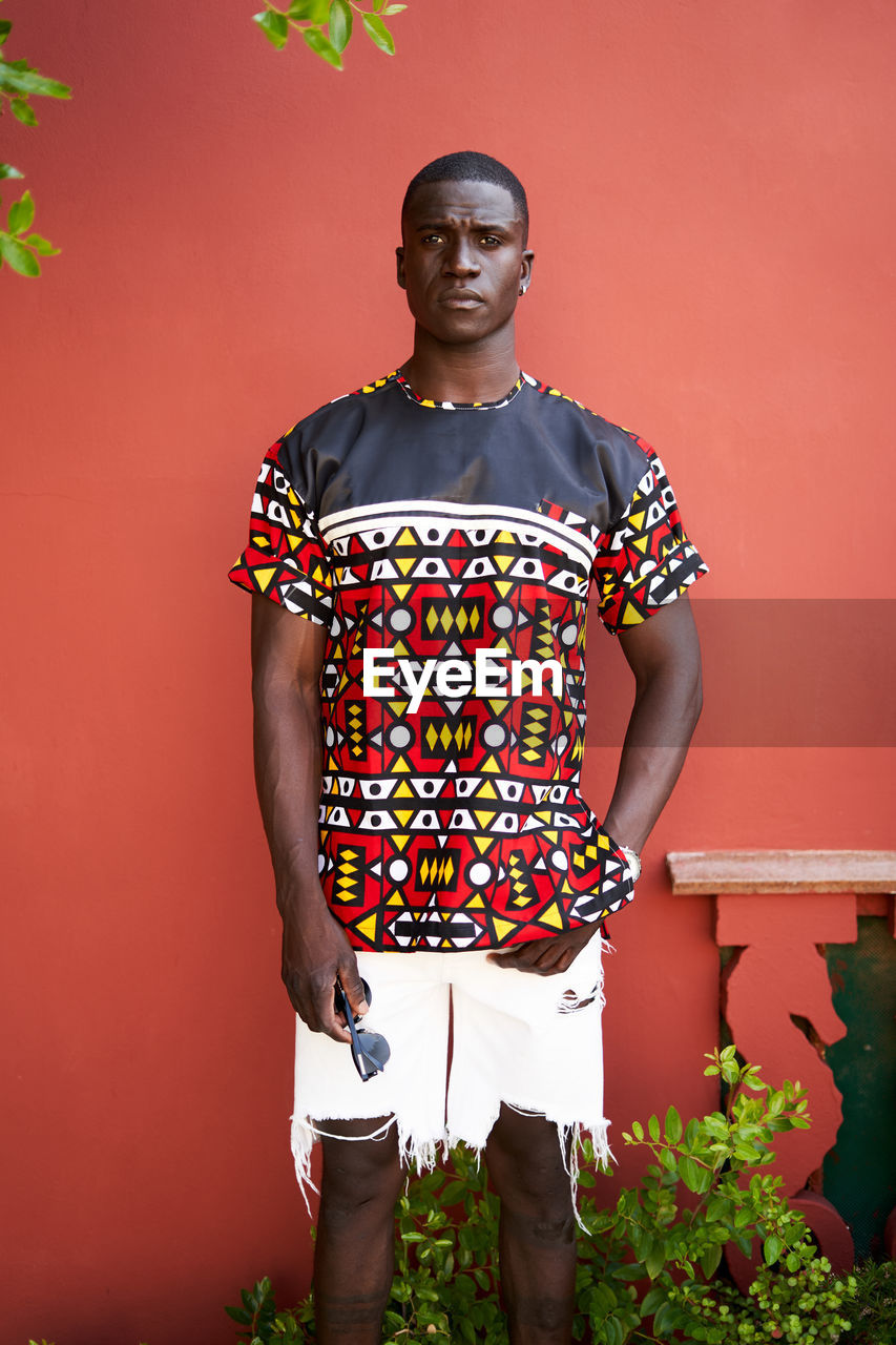 Content african american male in casual wear looking at camera against red background on street with plants