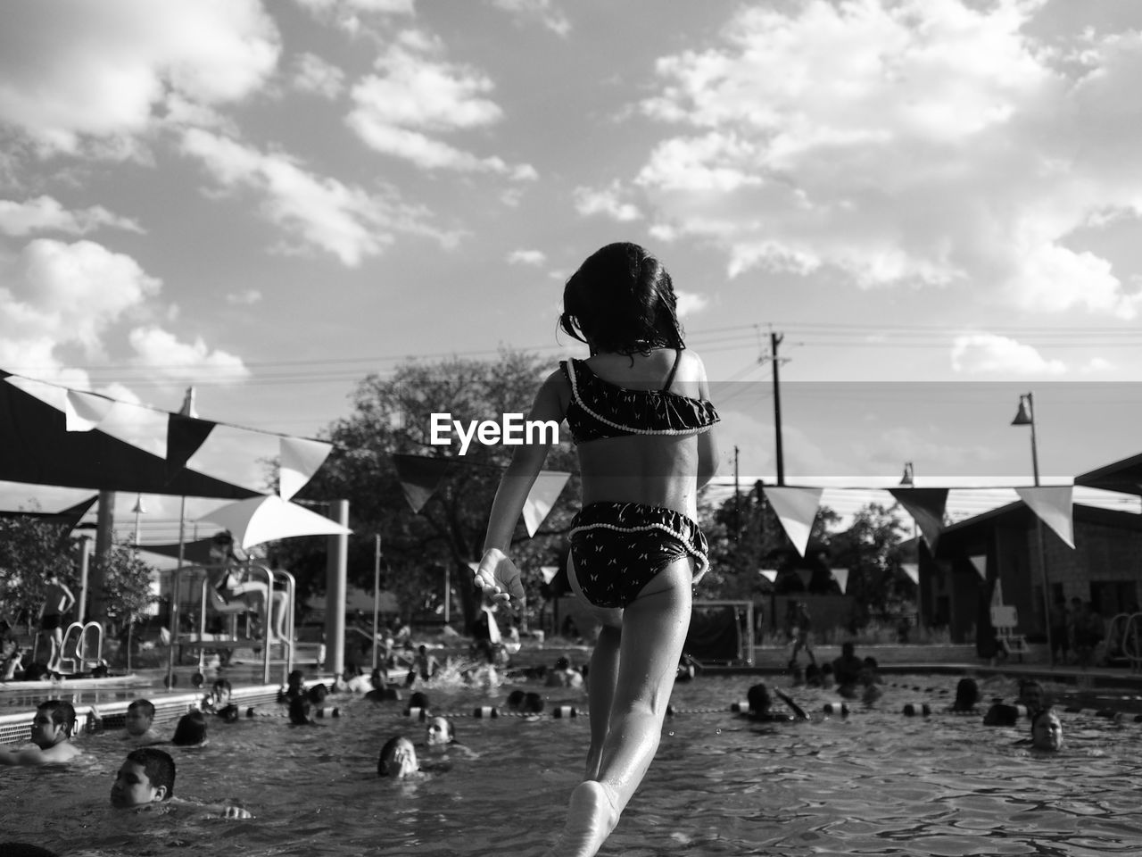 Rear view of girl in bikini diving into pool against cloudy sky