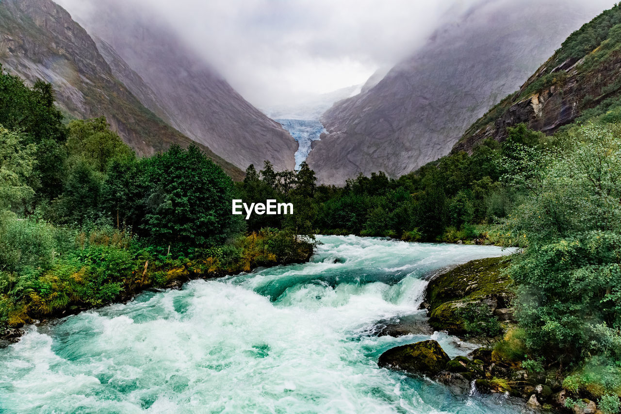 Scenic view on briksdal glacier, river and norwegian mountains against cloudy dramatic sky