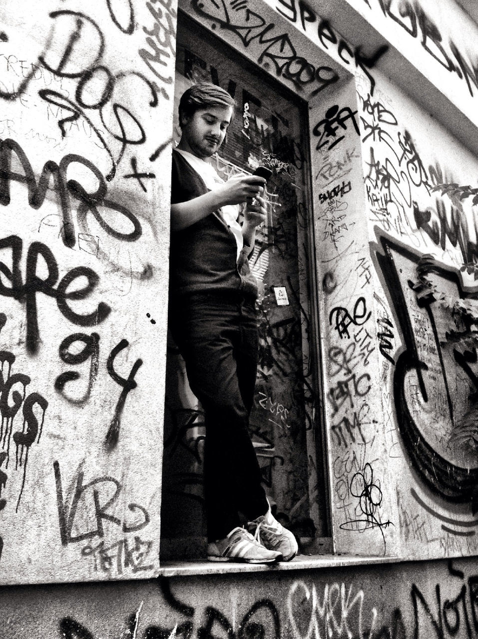 Full length of young man using mobile phone while leaning on graffitied wall
