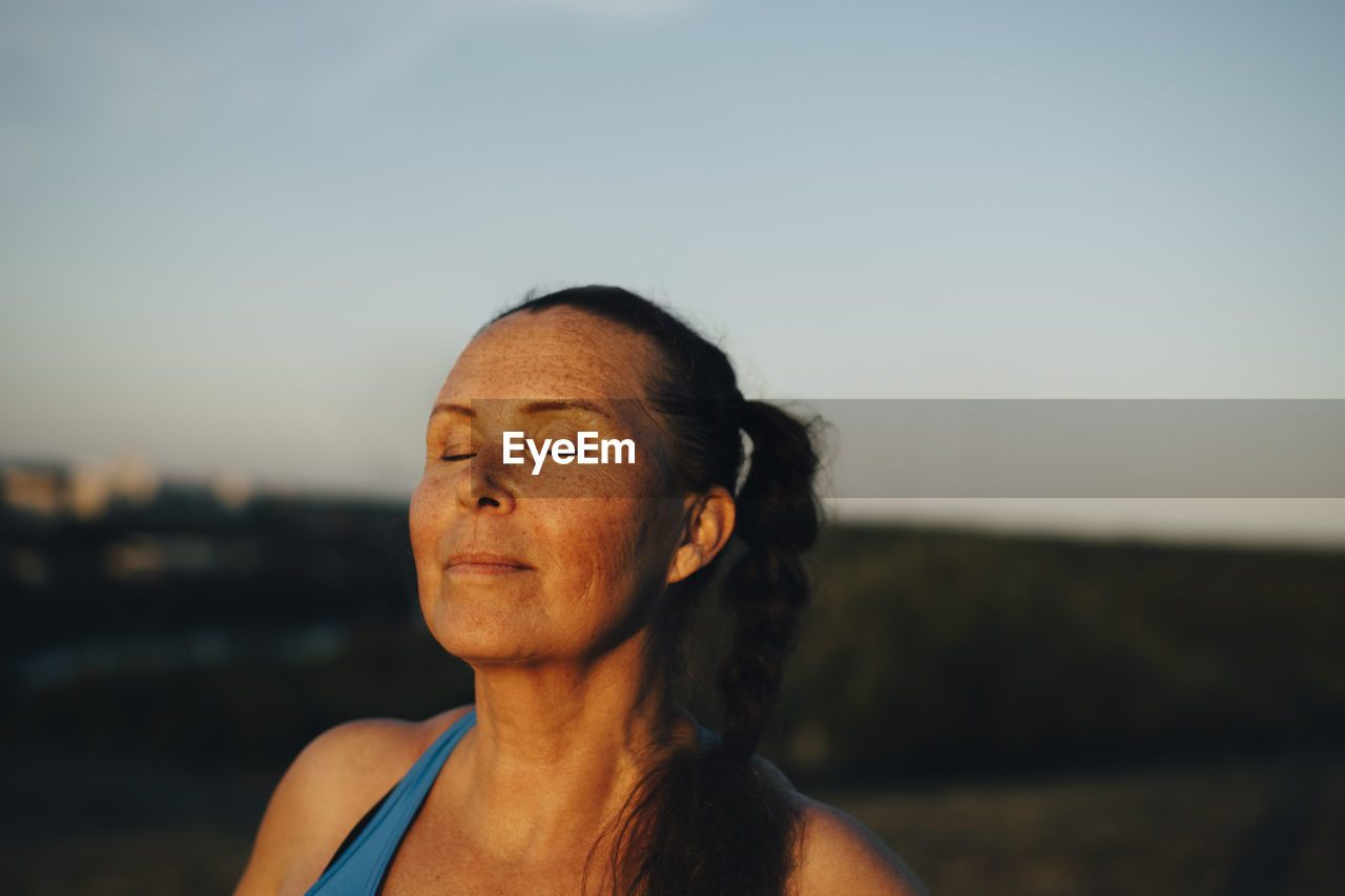 Sportswoman with eyes closed against sky during sunset