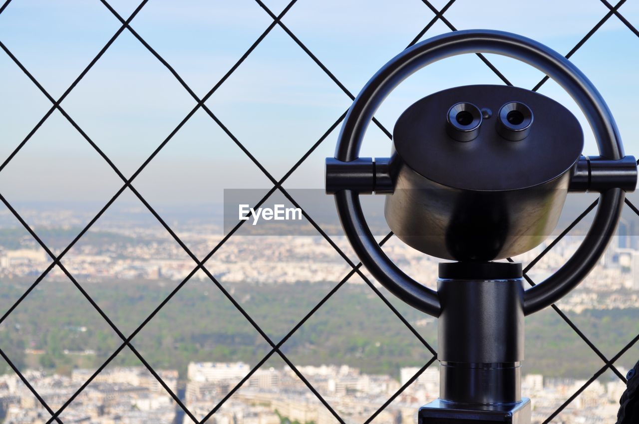 Coin-operated binoculars by fence at eiffel tower against sky