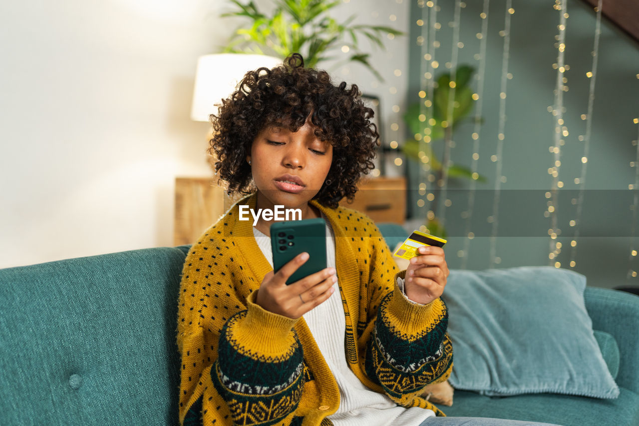 young woman using mobile phone while sitting on sofa at home