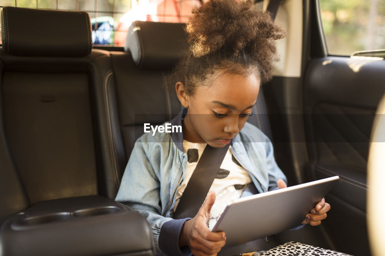 Girl using digital tablet while sitting in electric car