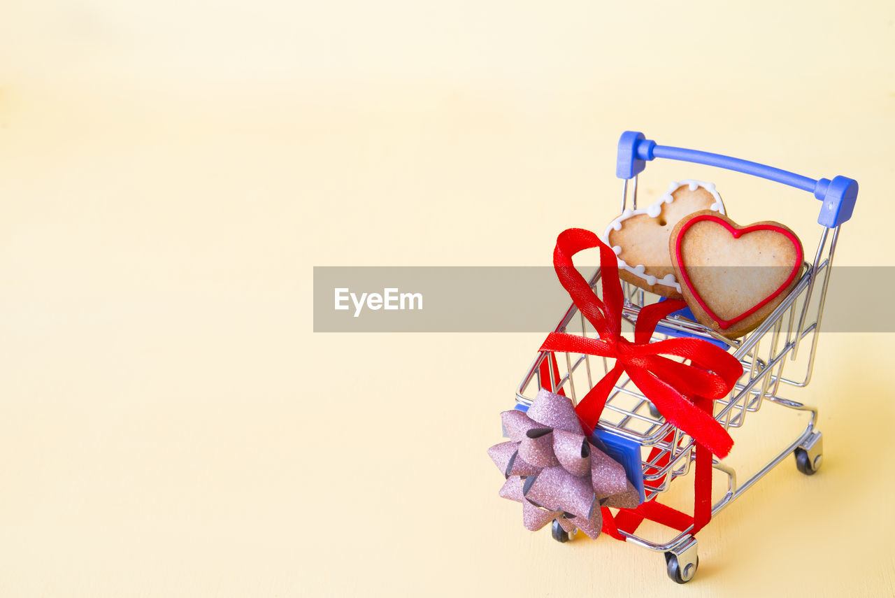 Close-up of heart shape cookies in small shopping cart against yellow background