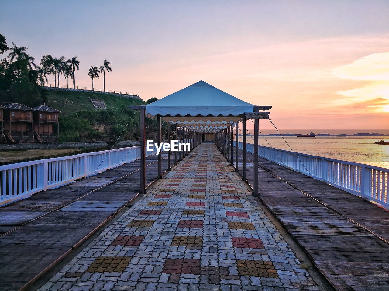 Walkway by sea against sky during sunset