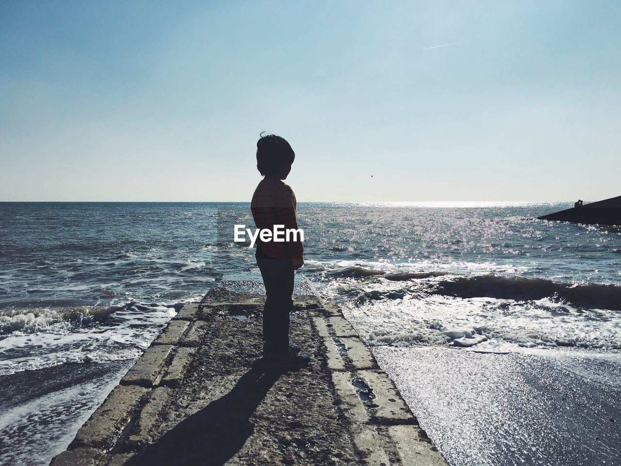 Rear view of boy walking on the beach against clear sky 