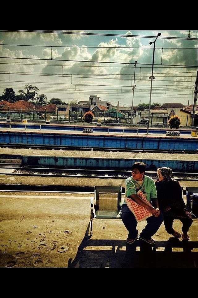 REAR VIEW OF WOMAN SITTING ON RAILROAD TRACK