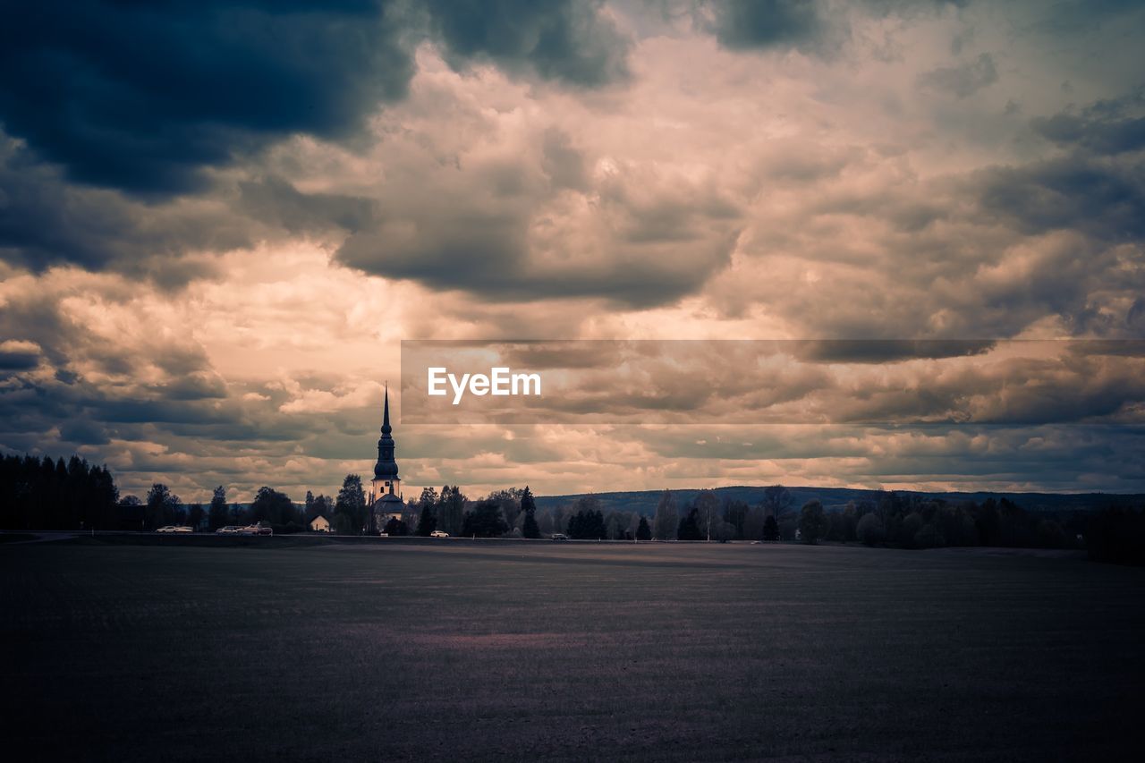 Distant view of stora tuna church on field against cloudy sky at dusk