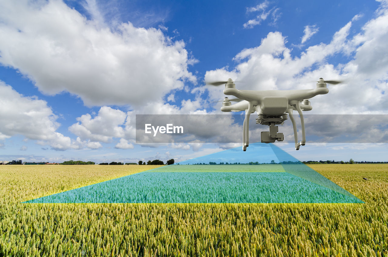 Drone flying over agricultural field against sky