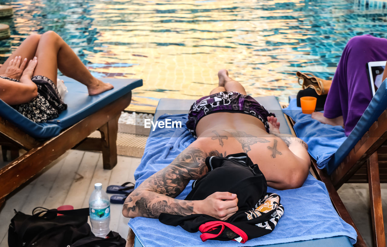 High angle view of tattooed man relaxing on lounge chair by swimming pool