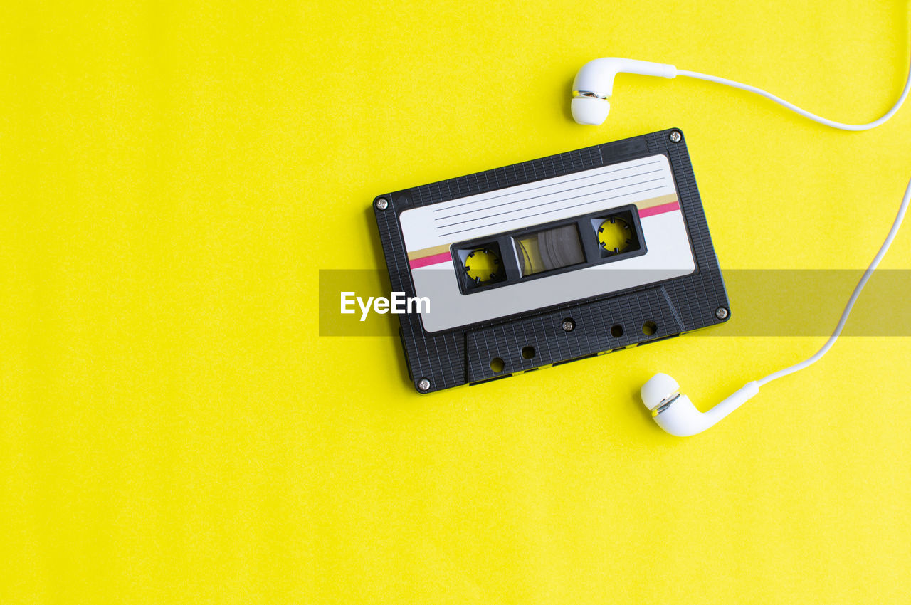 Directly above shot of audio cassette and in-ear headphones on yellow background