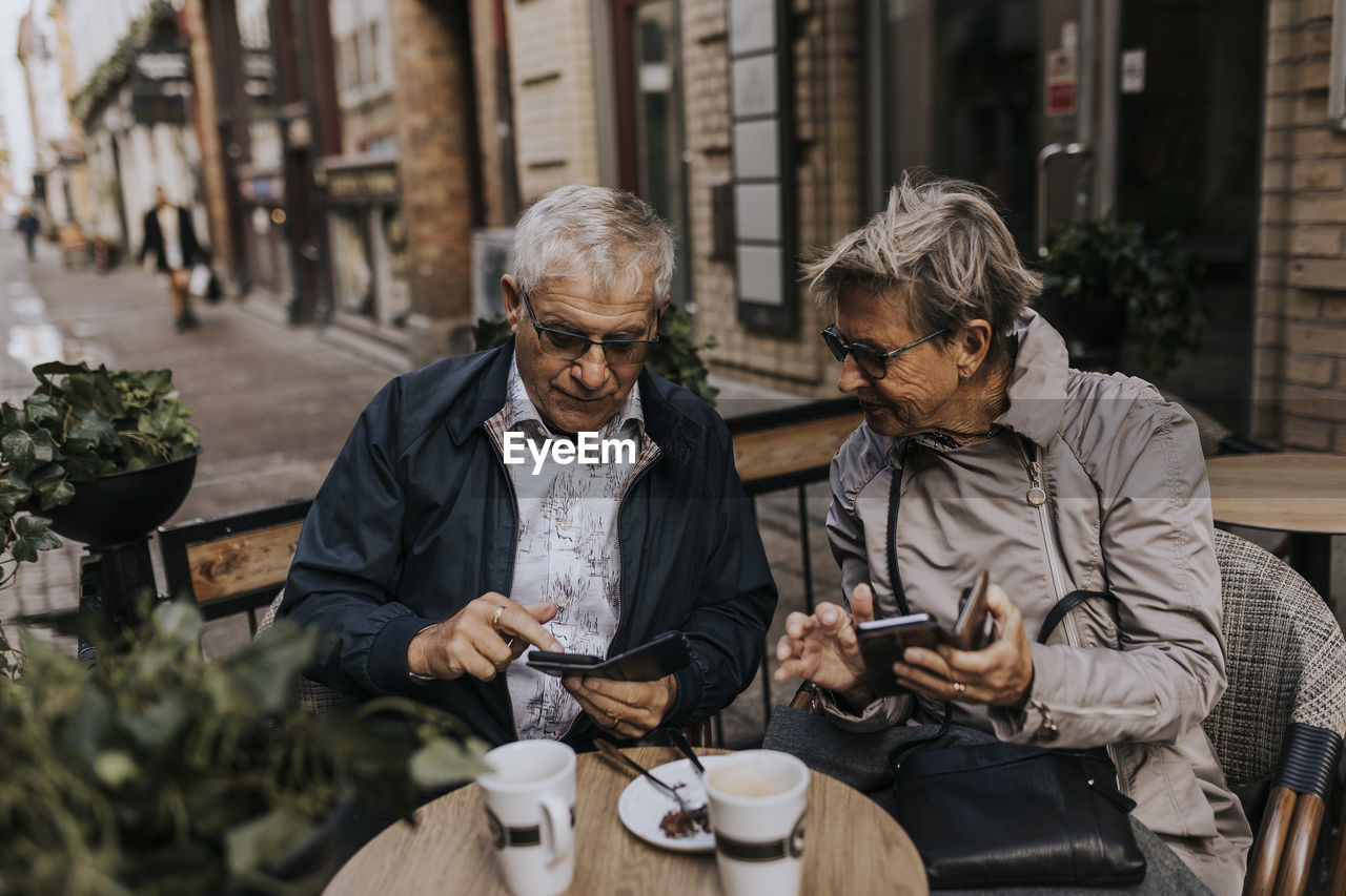 Senior couple using phones in sidewalk cafe