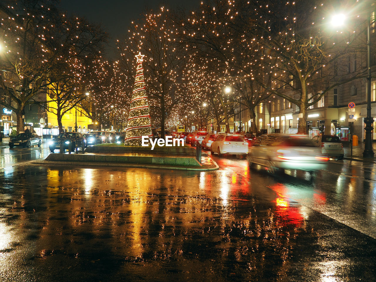 ILLUMINATED STREET BY BUILDINGS DURING RAINY SEASON