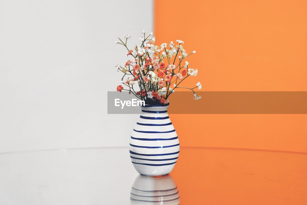 Flower vase against white and orange wall on table