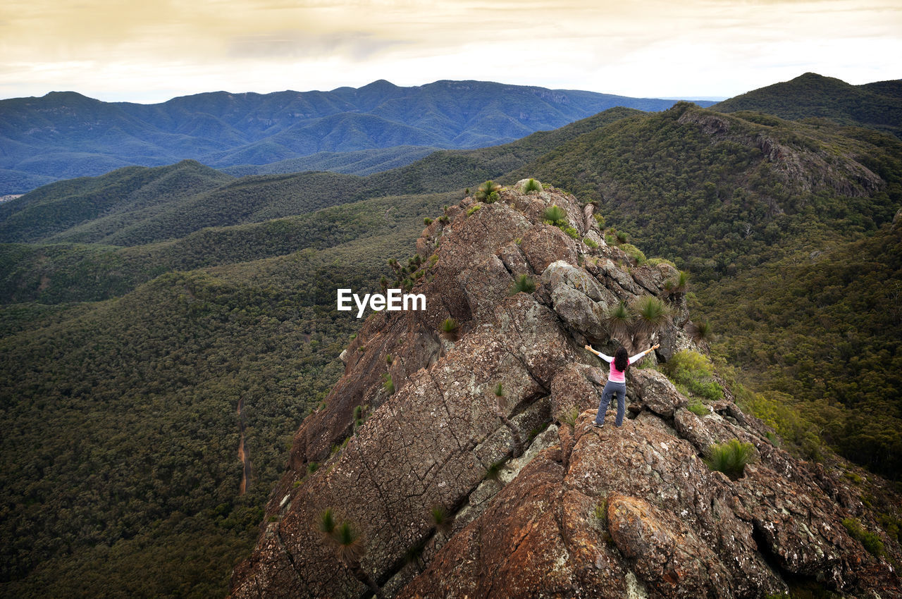 High angle view of woman with arms raised standing on mountain against sky