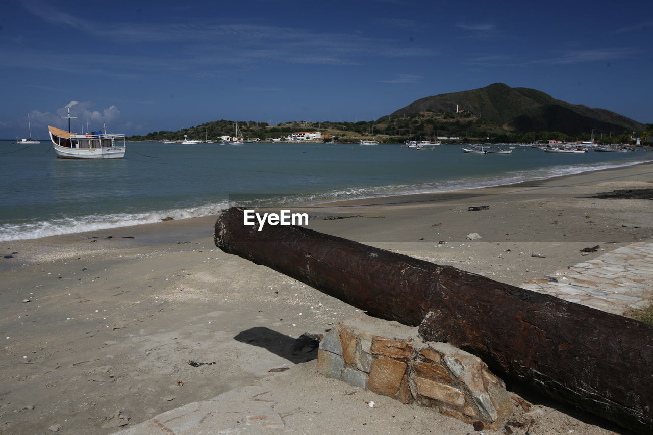 Rusty canon at beach against sky