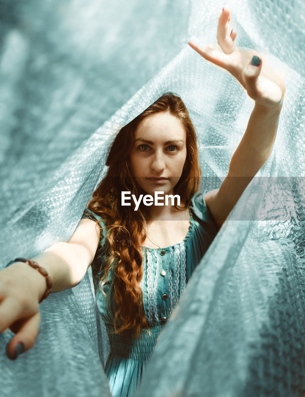 Portrait of beautiful young woman with arms raised standing amidst bubble wrap