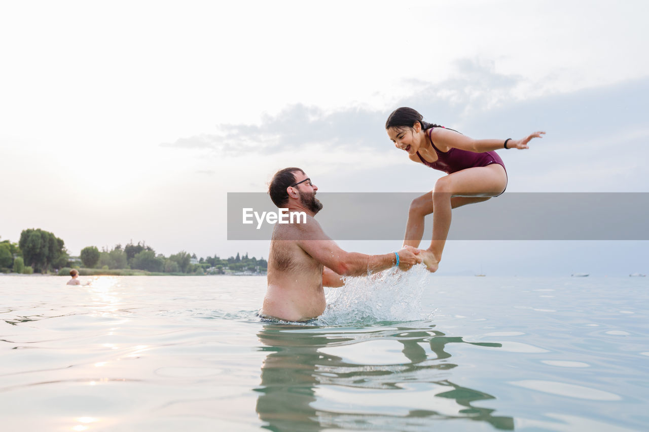 Side view at happy girl jumping in the water from the father arms