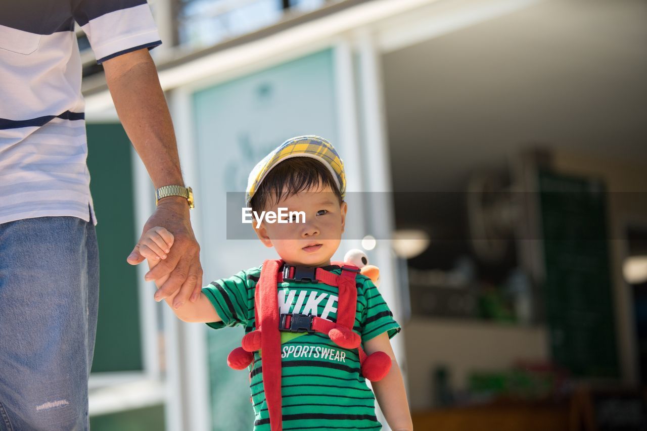 Midsection of father holding cute son hand while standing outdoors