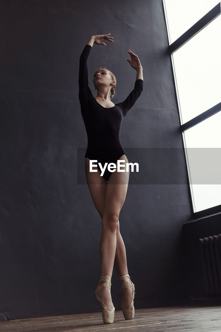A ballerina in a bodysuit and pointe shoes moves around the room with long strides
