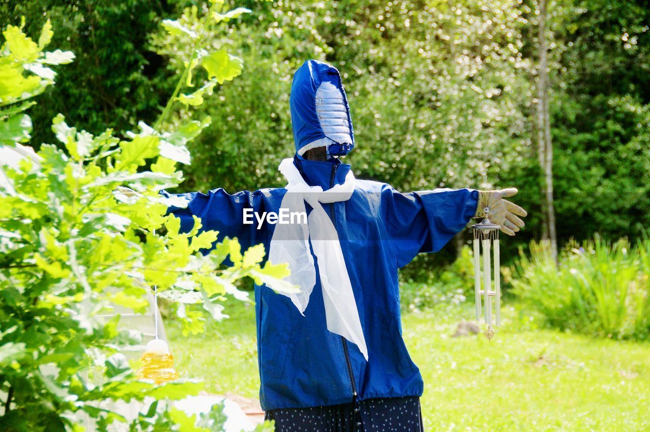 MIDSECTION OF PERSON WEARING MASK STANDING AGAINST TREES