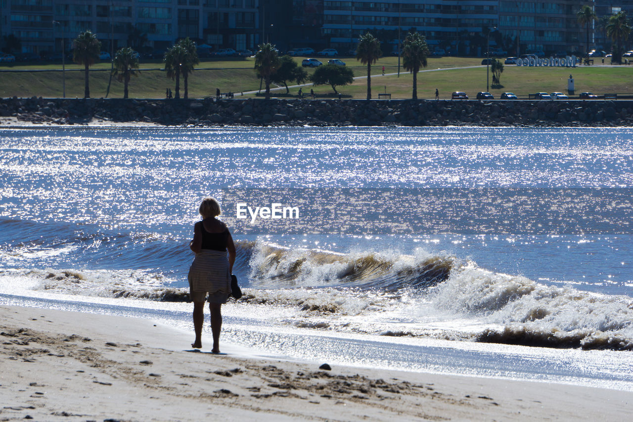 REAR VIEW OF MAN STANDING AT BEACH