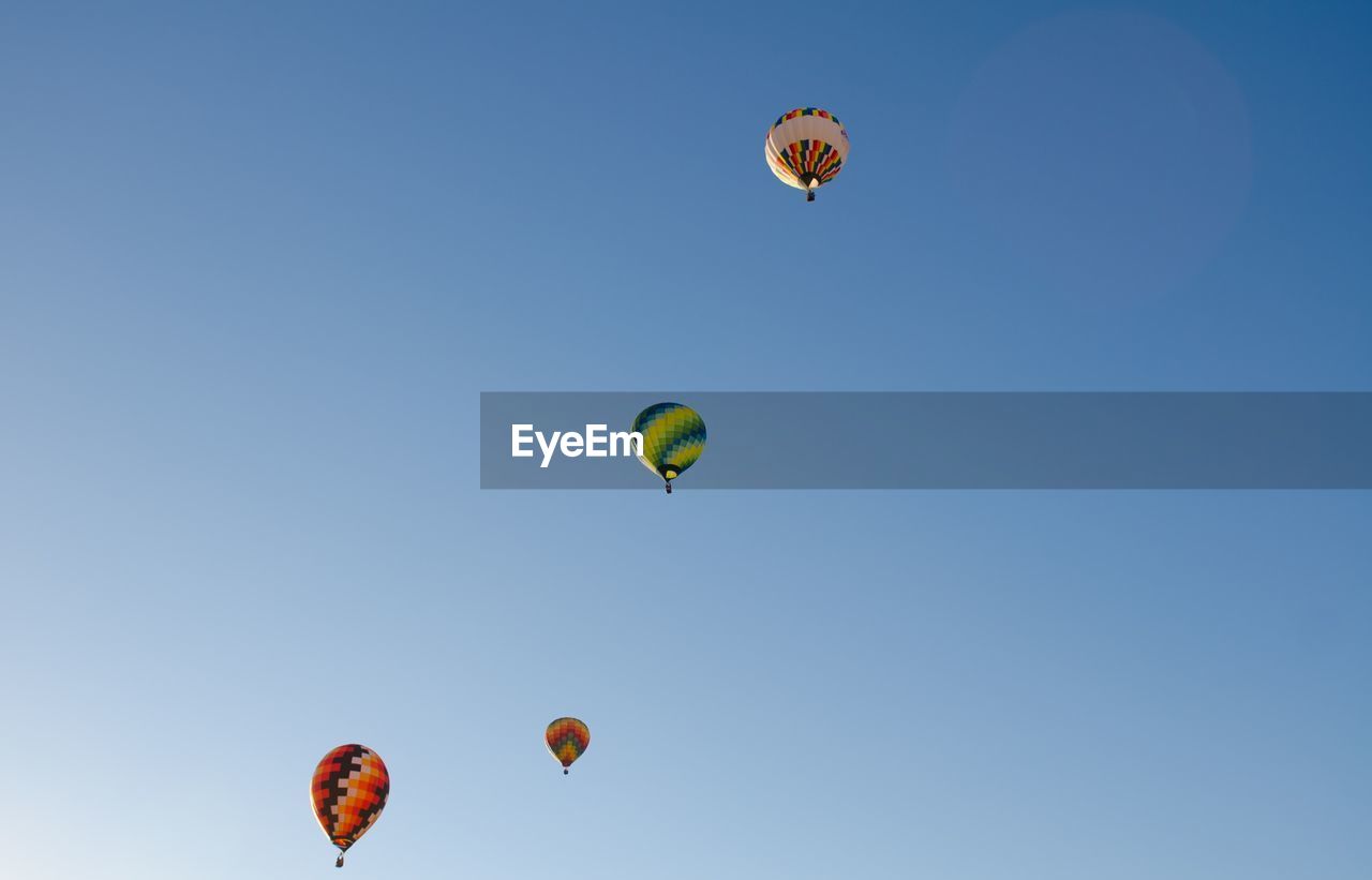 Low angle view of hot air balloons flying against clear blue sky