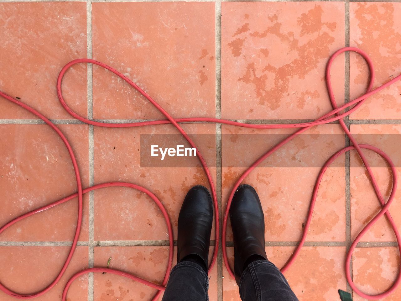 Low section of person standing amidst red cable on footpath