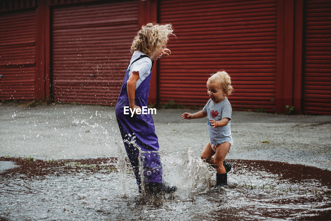 Girl and boy splashing in the water after the rain and laughing