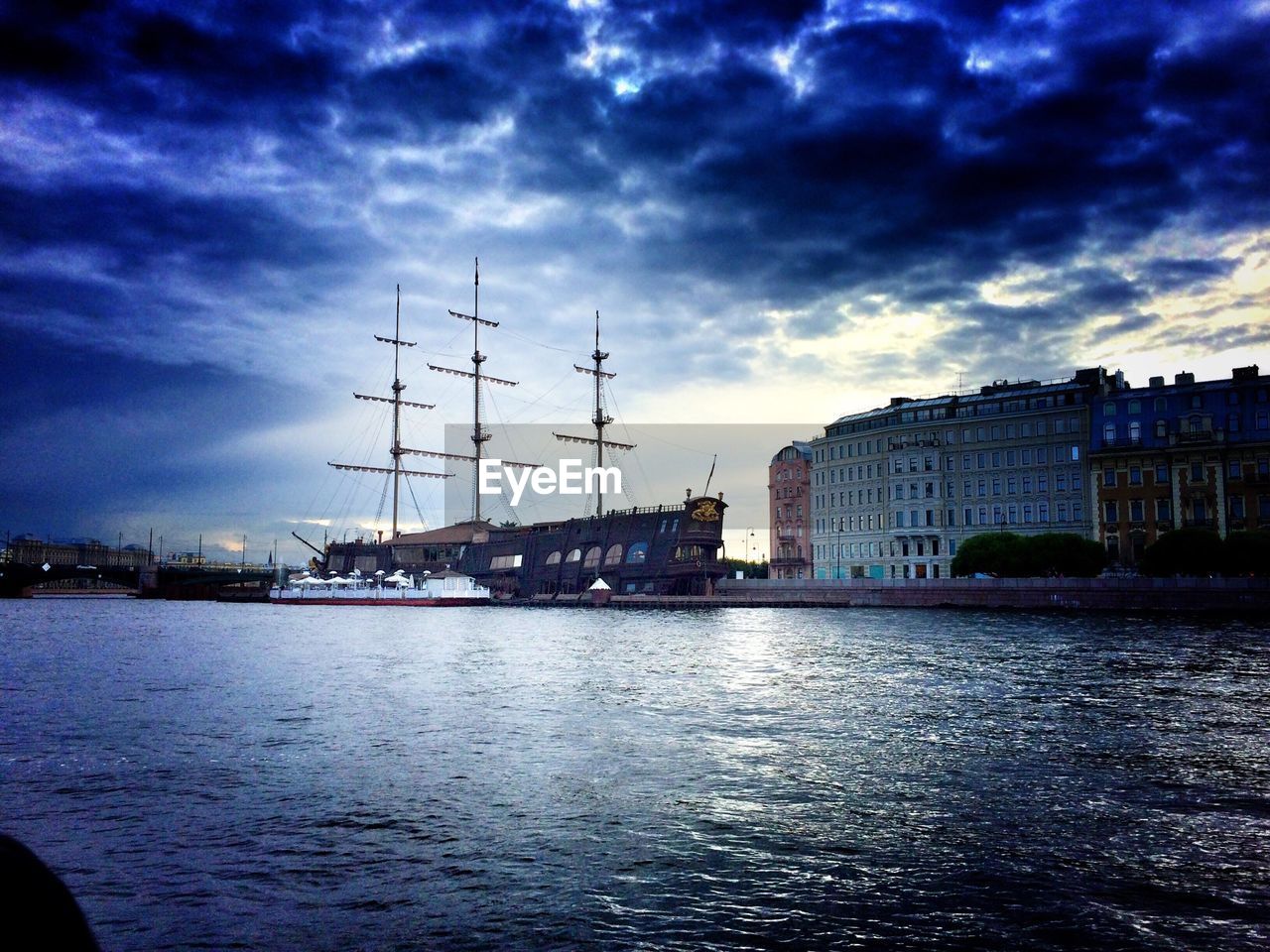 Ship on neva river by buildings against cloudy sky