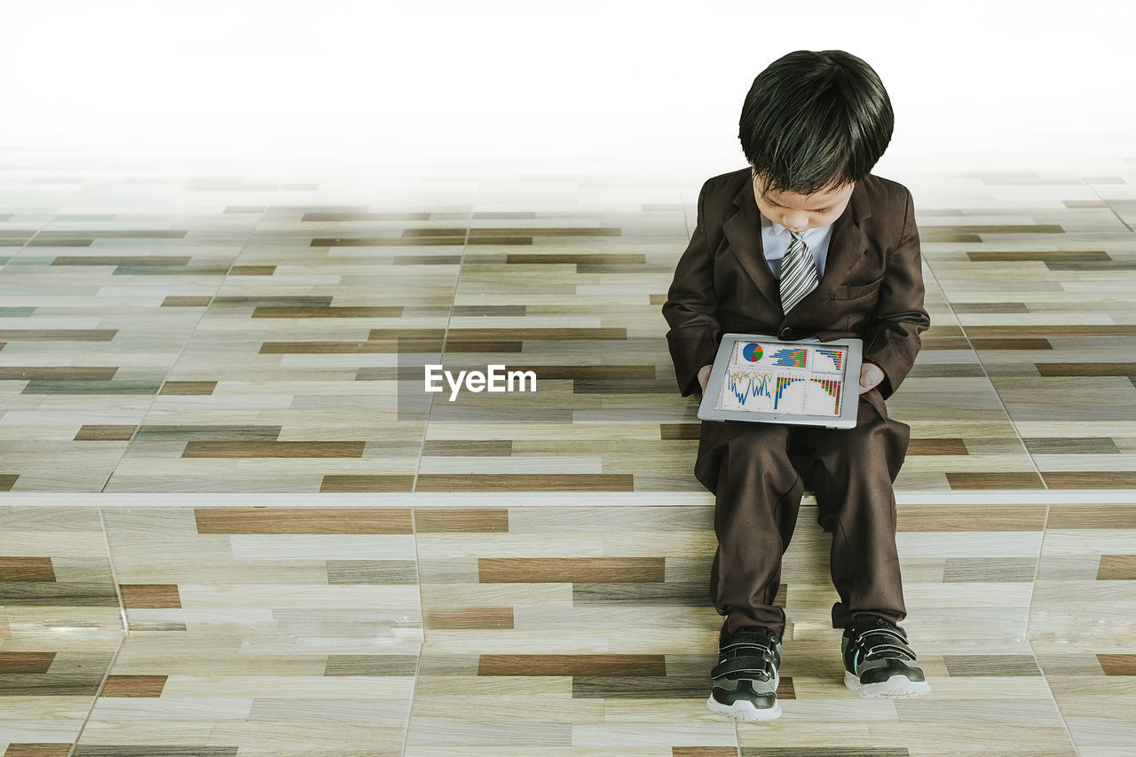 Boy in suit using digital tablet while standing on steps