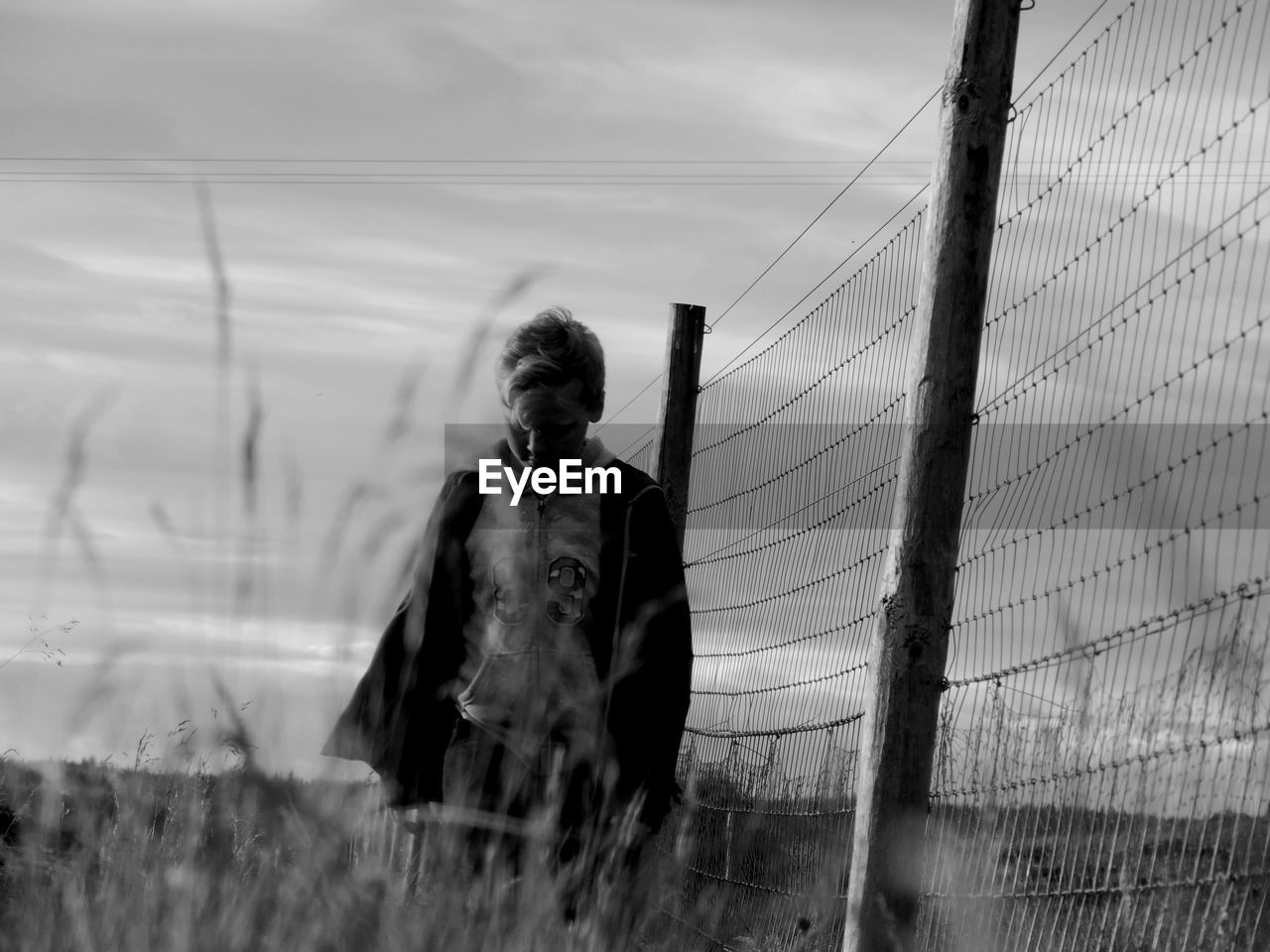 Boy standing by fence against sky