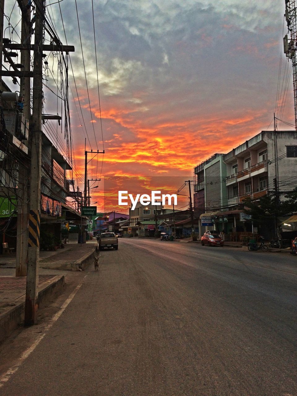 Road amidst buildings against sky at sunset