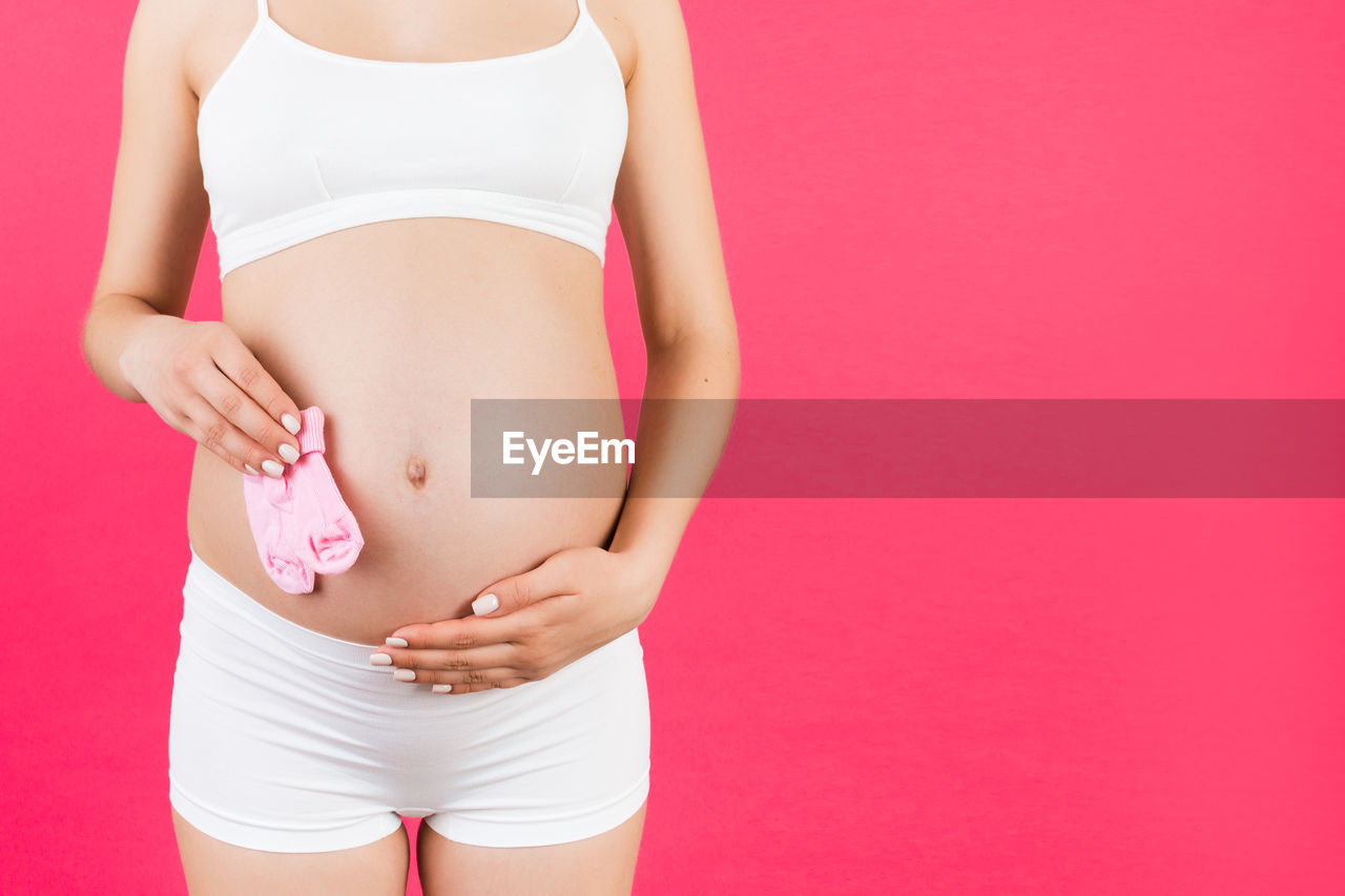 LOW SECTION OF WOMAN STANDING ON PINK OVER RED BACKGROUND