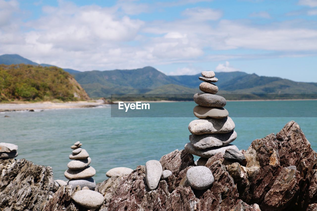Stack of stones on rocks by sea against sky