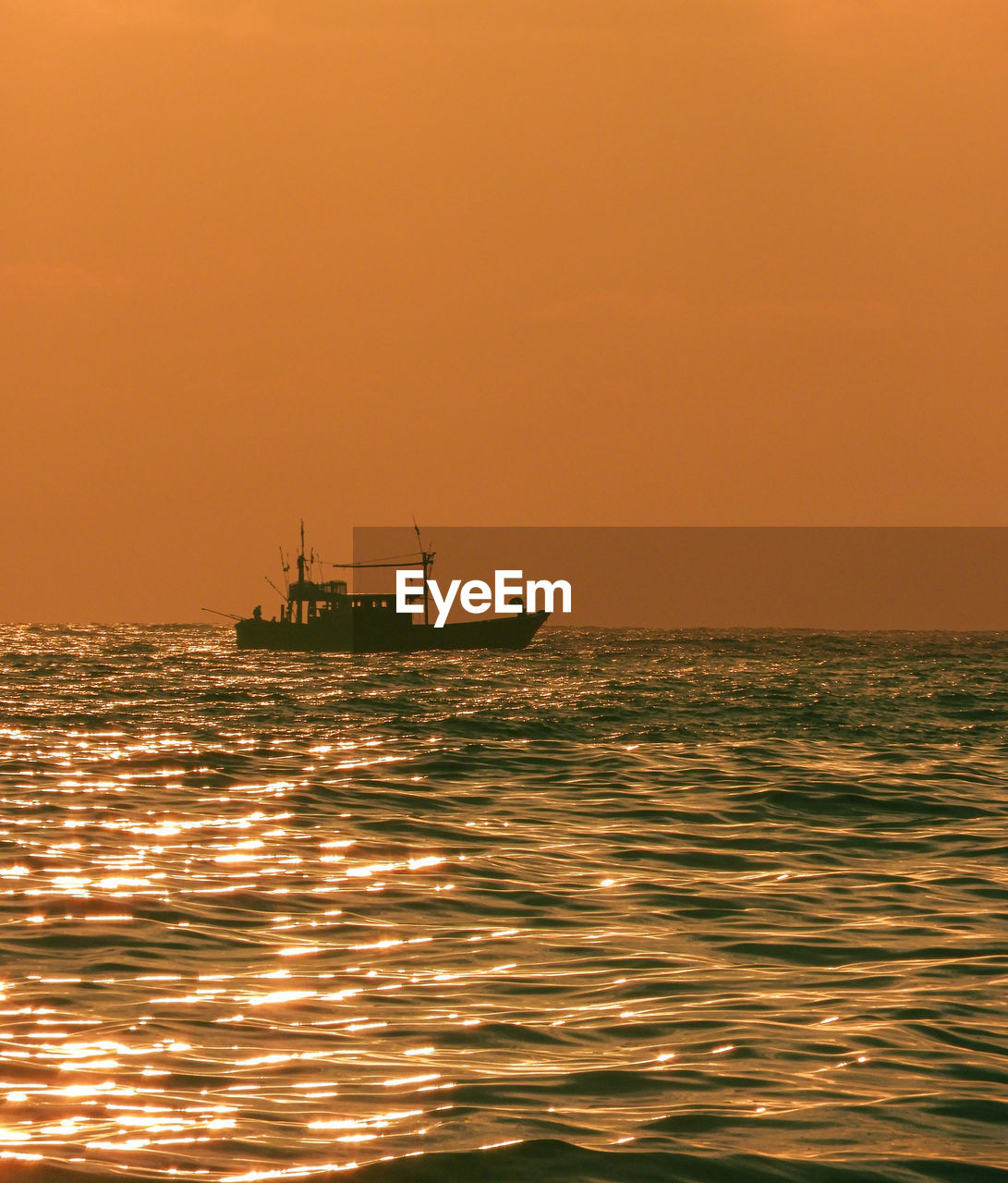 BOAT SAILING IN SEA AGAINST ORANGE SKY