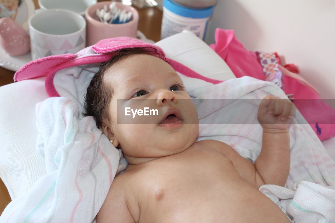 Close-up of shirtless baby girl lying on bed