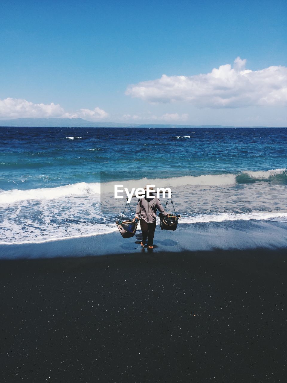 Full length of vendor with baskets at beach against sky