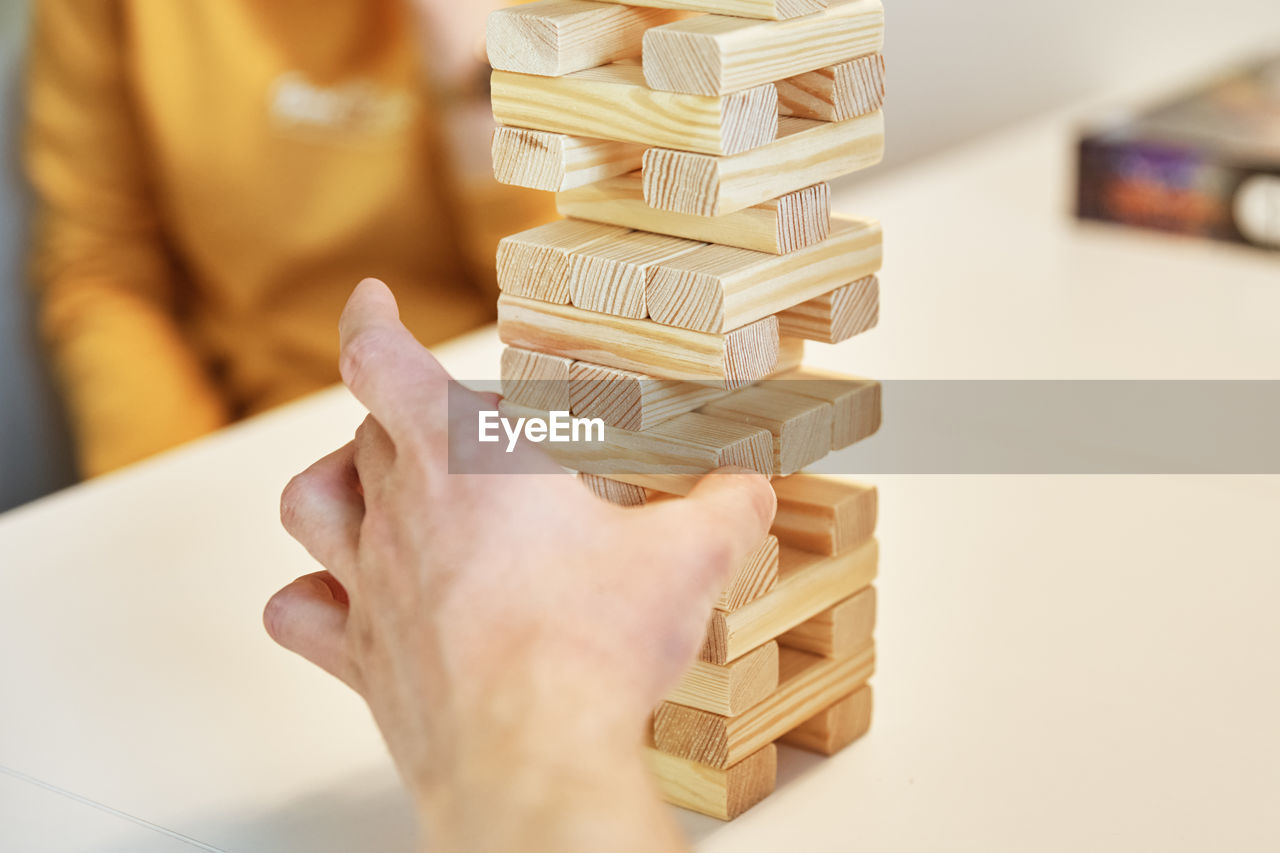 Family play board game. hands take wooden block from tower.