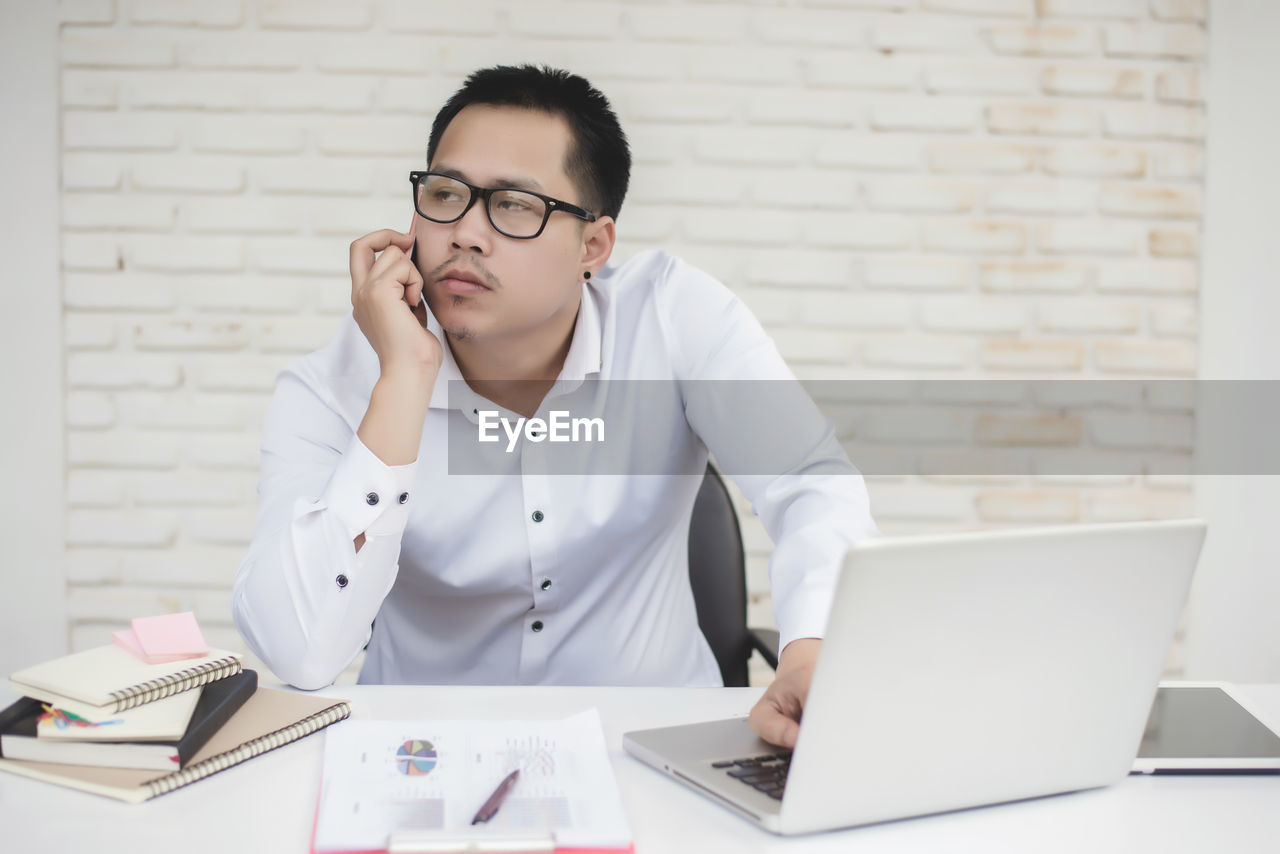 YOUNG MAN USING MOBILE PHONE ON TABLE