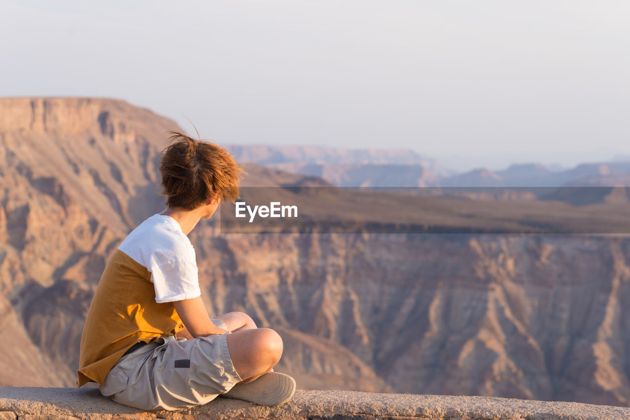 Woman sitting on mountain while looking at view