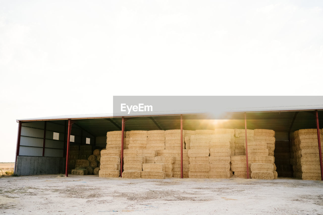 Industrial shelter with stacked hay rolls in remote agricultural fields of sunny countryside